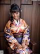 A woman in a kimono sitting on a wooden chair.