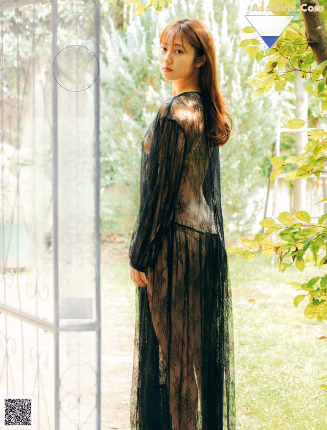 A woman in a black lace dress standing in front of a gate.