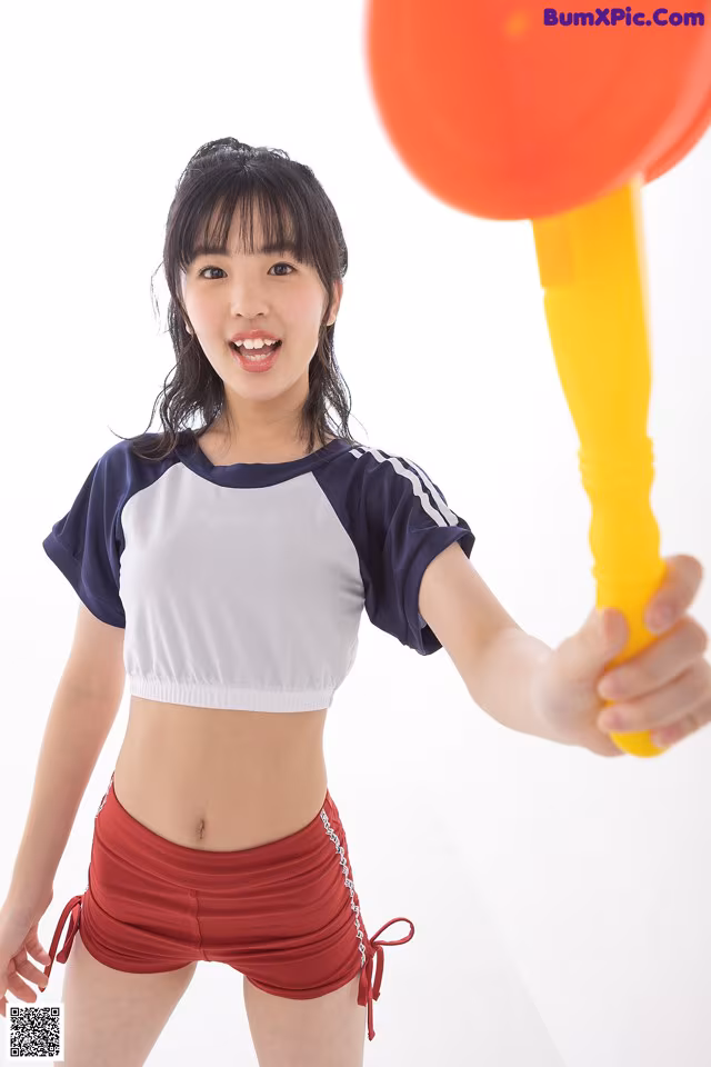 A woman in a white top and red shorts holding a red balloon.