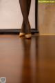 A woman in black stockings and high heels standing on a wooden floor.