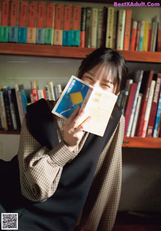 A woman sitting in front of a bookshelf holding a book.