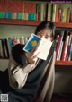 A woman sitting in front of a bookshelf holding a book.