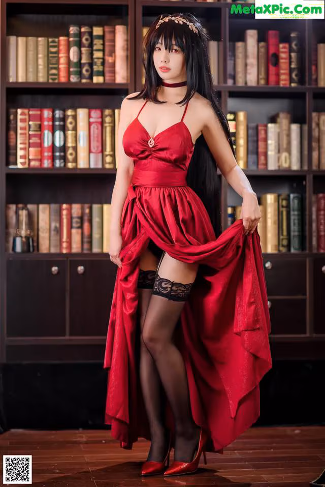 A woman in a red dress standing in front of a bookshelf.