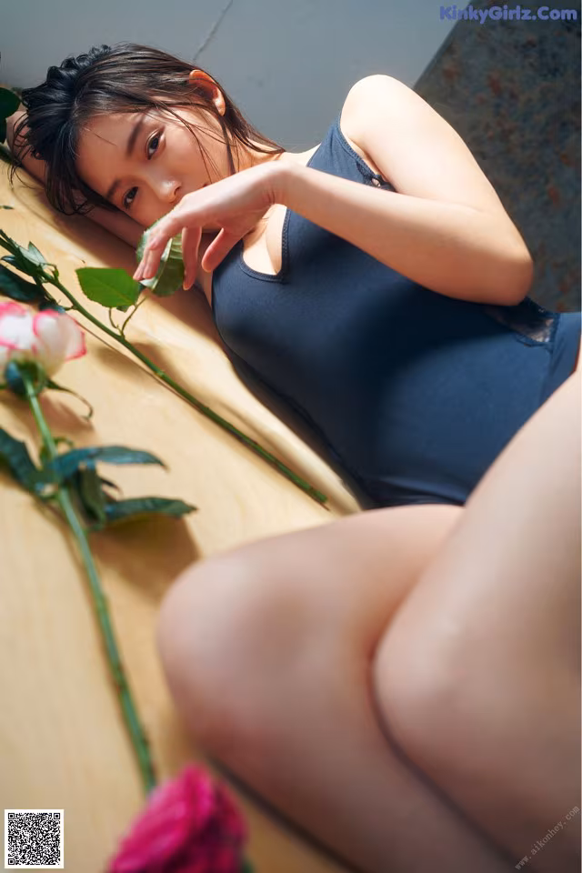 A woman laying on a bed next to a pink rose.