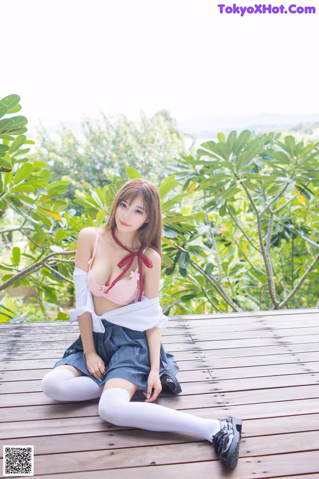 A woman sitting on a wooden deck in a pink top and skirt.