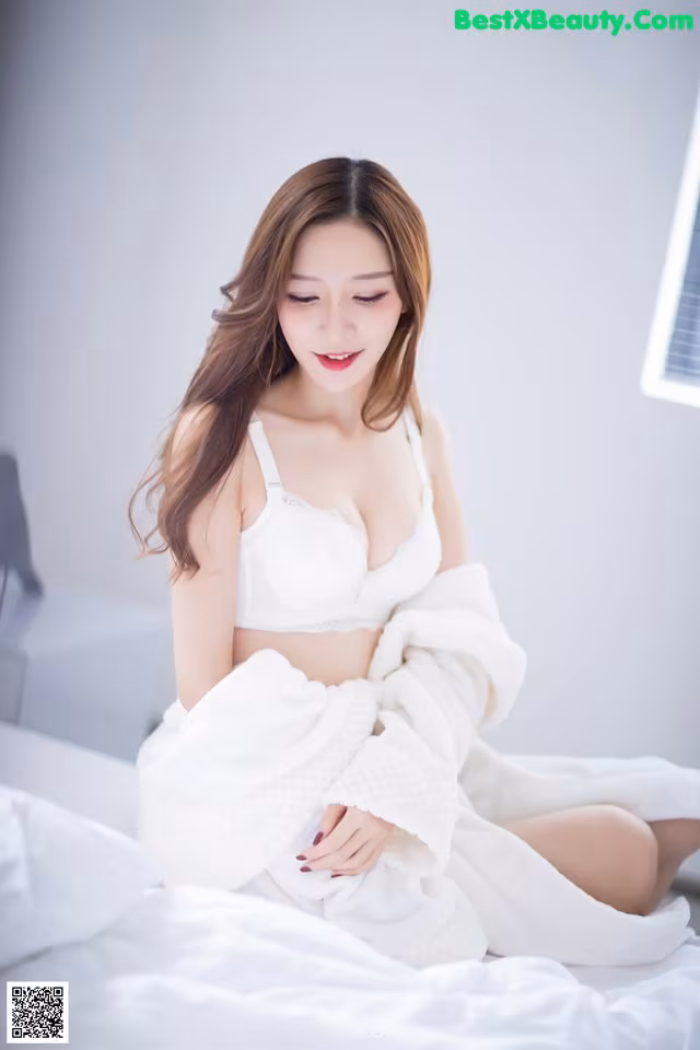 A woman sitting on a bed in a white robe.