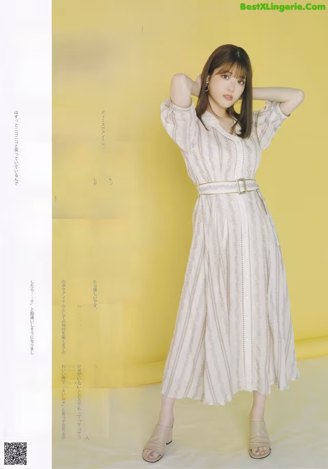 A woman in a white dress standing in front of a yellow wall.