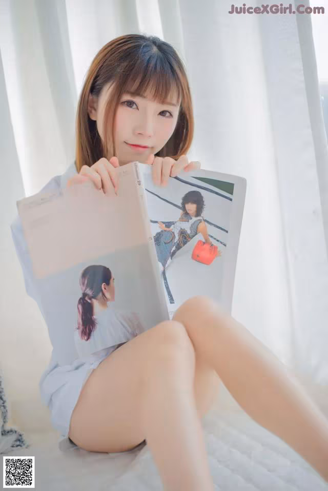 A woman sitting on a bed holding a magazine.