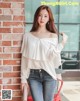 A woman leaning against a brick wall wearing a white blouse.