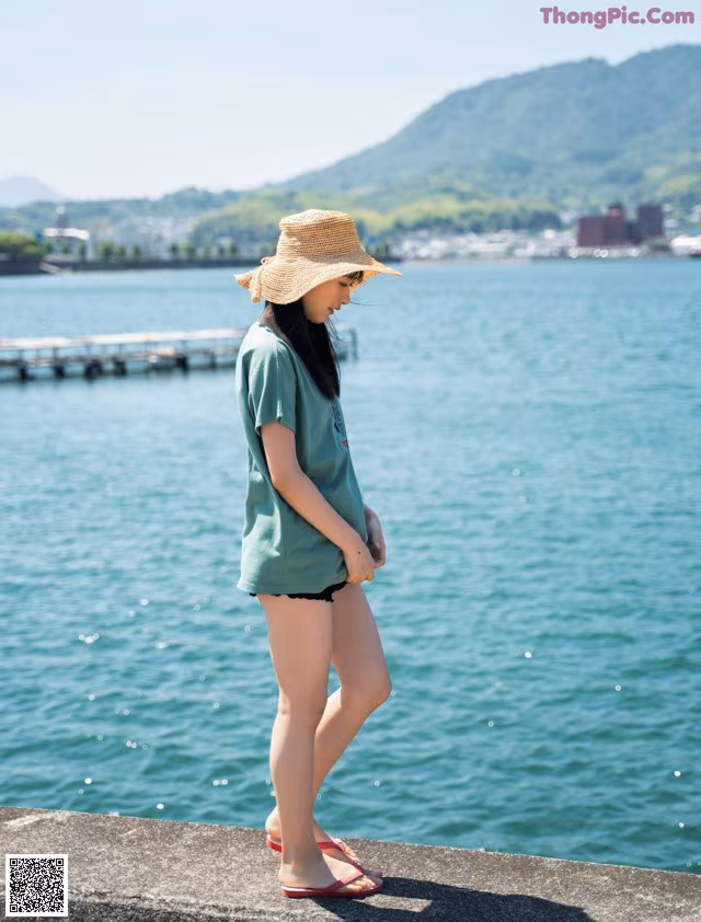 A woman wearing a straw hat standing by the water.