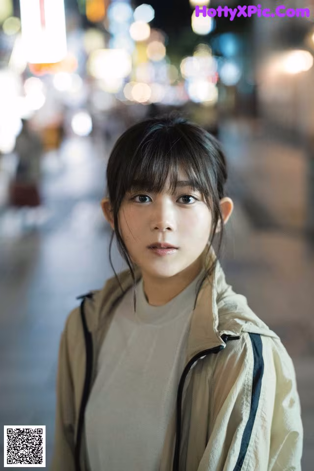 A young woman standing in the middle of a city at night.
