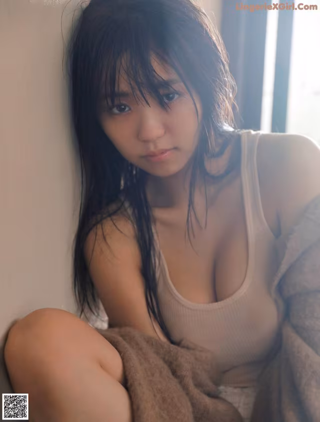 A woman sitting on a window sill with a towel around her neck.