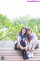 A couple of young women sitting on top of a wooden deck.