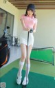 A woman in a pink shirt and white skirt holding a golf club.