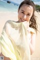 A woman in a bikini holding a yellow scarf on the beach.