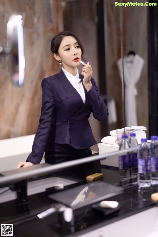 A woman in a purple suit is putting on lipstick.
