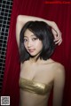 A woman in a gold bikini posing in front of a red curtain.