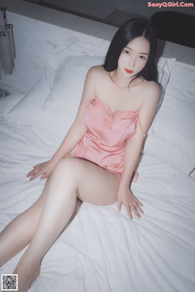 A woman in a pink dress sitting on a bed.