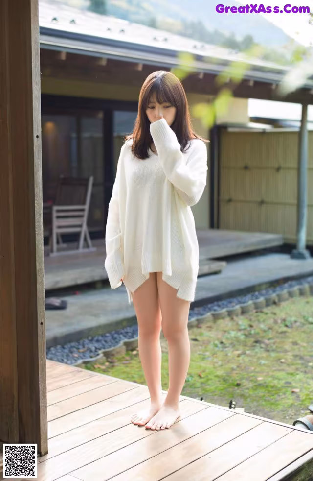 A woman in a white sweater standing on a wooden deck.